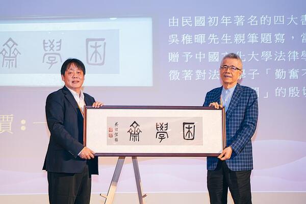 法律系60周年慶祝餐會上，由信義企業集團創辦人周俊吉校友（右）成功拍得「困學齋」畫作，以行動支持母系發展。左為王子奇校長。圖／法學院